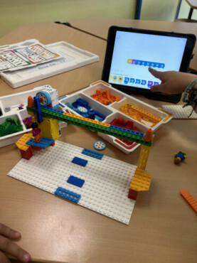 AG-Angebote an der Alteburgschule Lego-Modell auf einer weißen Grundplatte, daneben ein Tablet mit Programmieroberfläche und Lego-Sortierbox.