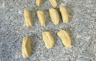 Kinderhände rollen und formen Hefeteig auf einer Arbeitsfläche.