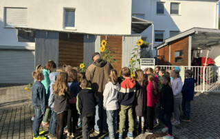 Gruppe von Kindern steht im Freien vor einer großen Sonnenblume.