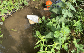 Mehrere kleine Boot-Modelle aus Kork und Holz schwimmen in einer orangefarbenen Schüssel voller Wasser.