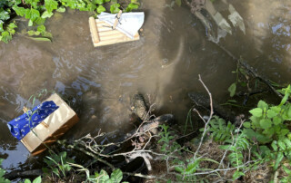 Kinderhand setzt ein Modellboot ins flache Wasser eines Bachs.