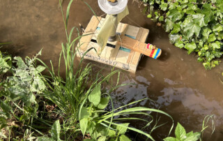 Buntes Bootmodell liegt im Bachlauf zwischen Grasbüscheln.