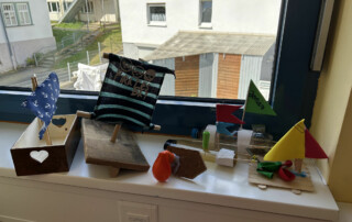 Kleine Modelle und Boote stehen auf einer Fensterbank vor Fenstern.