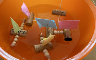 Mehrere selbstgebastelte Boote mit bunten Segeln stehen auf einer Fensterbank.