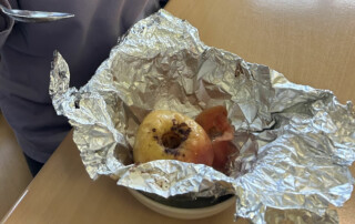 Kind hält einen Löffel über einem Bratapfel, der in Alufolie liegt.