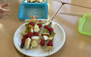 Kinderhände greifen nach Obstspießen auf einem gedeckten Tisch.