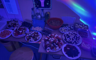 Hand greift nach einem Teller mit Obstspießen aus Melone, Trauben und Banane.