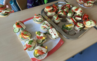 Tablett mit belegten Brötchenhälften, garniert mit Gemüse und Kräutern.