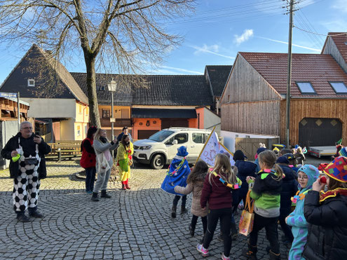 Gruppe von Kindern steht im Freien auf einem Platz und nimmt an einer Veranstaltung teil.