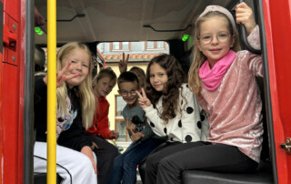 Kinder sitzen nebeneinander auf den Sitzen eines Feuerwehrfahrzeugs.