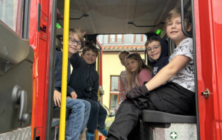 Kinder sitzen im Mannschaftsraum eines Feuerwehrautos und schauen nach außen.