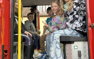 Kinder sitzen im Inneren eines Feuerwehrfahrzeugs auf den hinteren Sitzen.