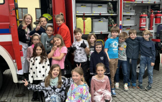 Kinder stehen vor einem geöffneten Feuerwehrfahrzeug und betrachten die Ausstattung.