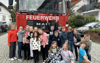 Kinder stehen auf einem Platz vor einem Feuerwehrfahrzeug.