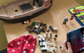 Kind spielt mit kleinen Tierfiguren und einem Spielzeugschiff auf einem Tisch.