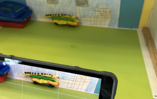 Knetfigur und kleines Bastelmotiv liegen vor einer farbigen Pappe als Kulisse.