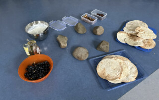 Teller mit Fladenbrot, Schalen mit Bohnen, Datteln und weiteren Zutaten auf einem Tisch.