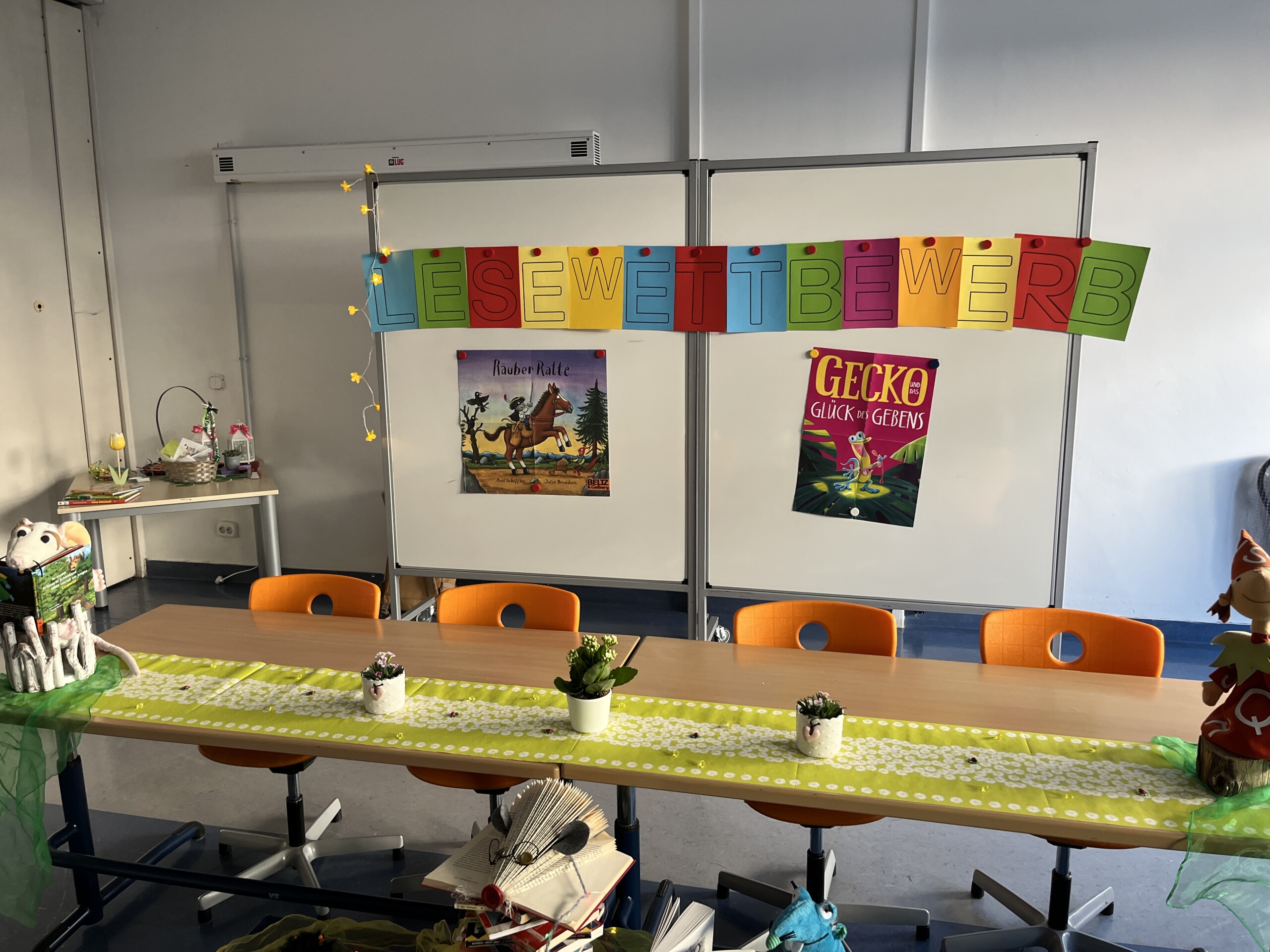 Ausstellung gestalteter Blätter an einer weißen Wand unter einer bunten Girlande.