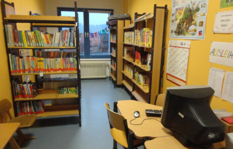 Innengebäude Schulbücherei mit Regalen voller Bücher, einem Computerarbeitsplatz
