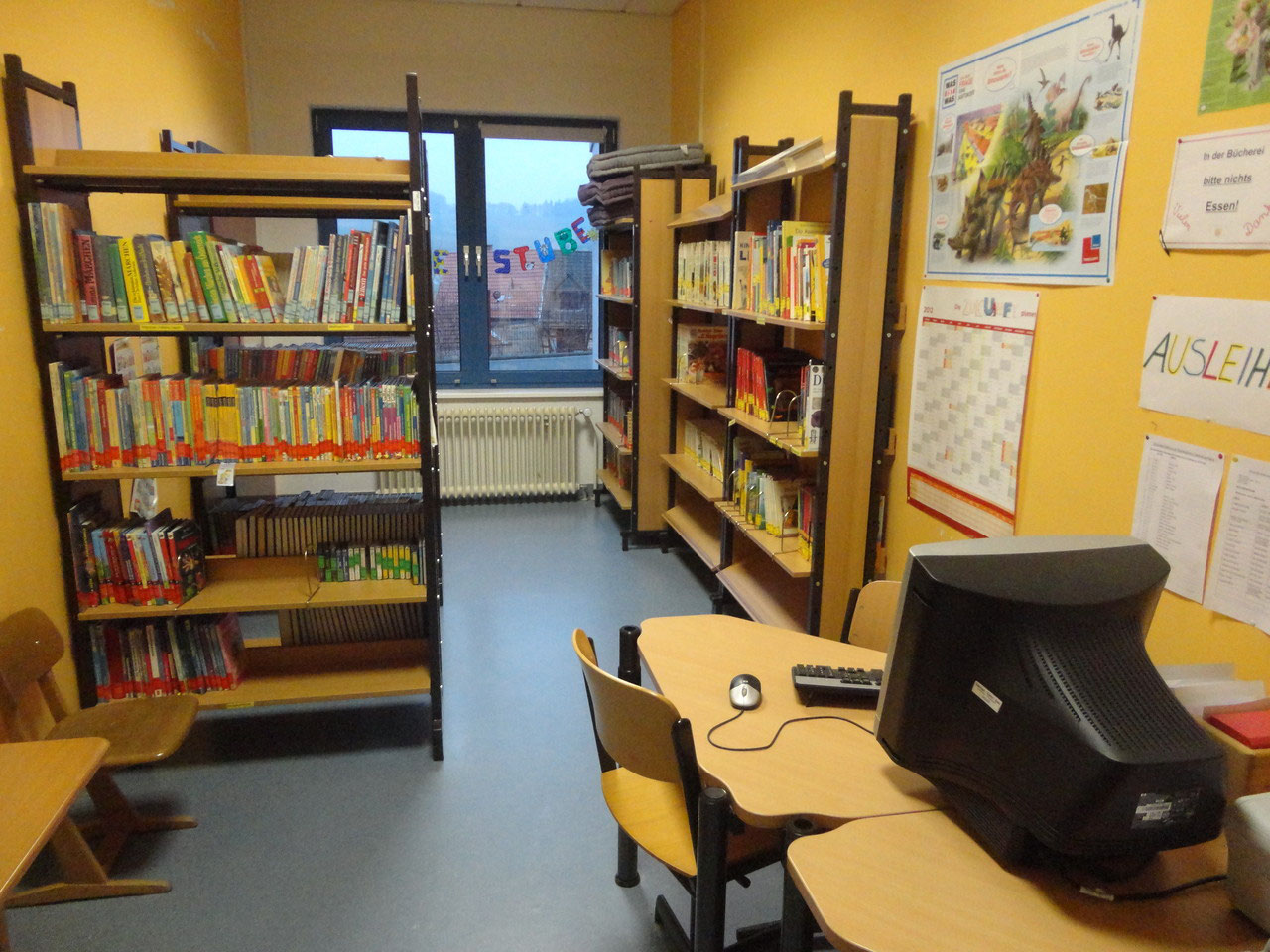 Schulbücherei mit Regalen voller Bücher, einem Computerarbeitsplatz