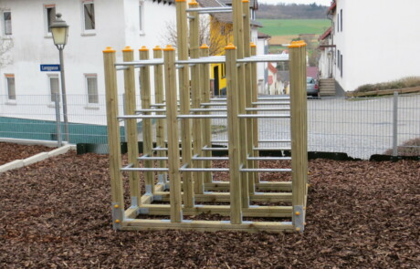 Pausenhof Klettergerüst aus Holz neben blau-gelben Pfosten auf dem Schulhof.