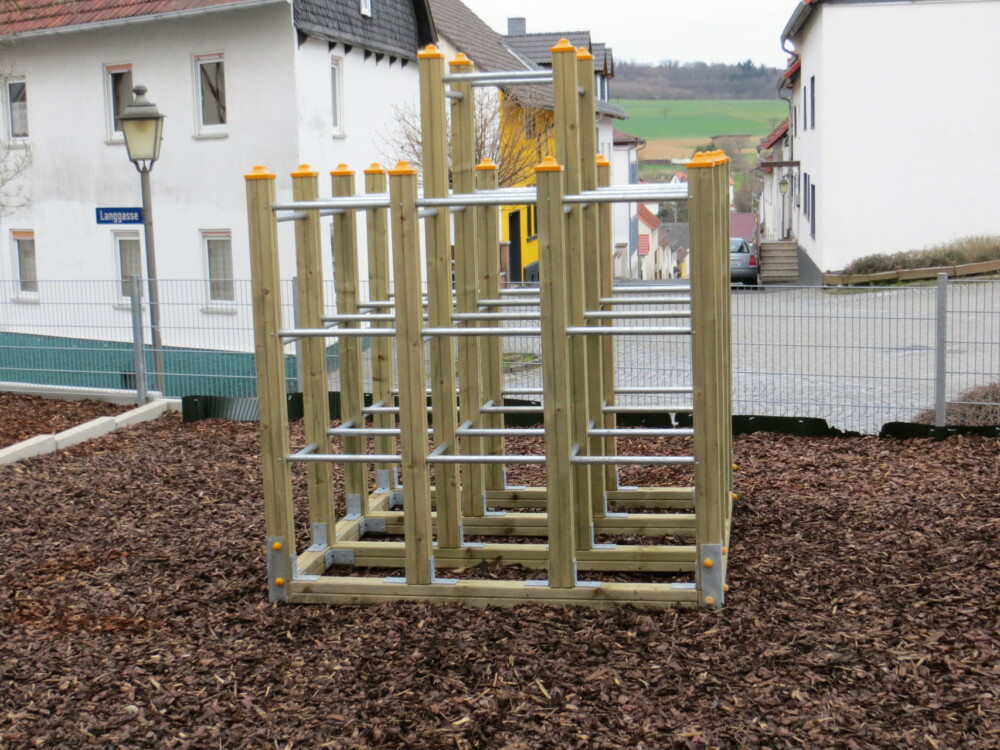 Klettergerüst aus Holz neben blau-gelben Pfosten auf dem Schulhof.