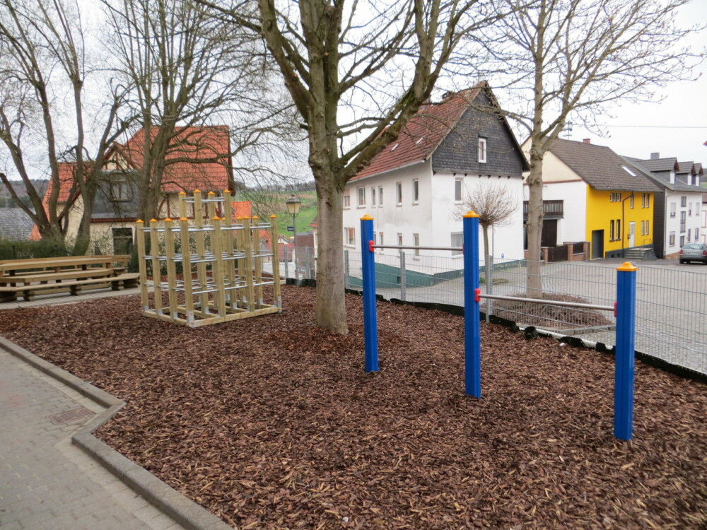 Spielplatz mit Klettergerüst und blau-gelben Pfosten auf Rindenmulch.