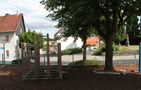 Pausenhof Spielplatzbereich mit Klettergerüst neben schattigen Bäumen.