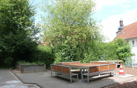 Pausenhof Bereich des Schulhofs mit Bäumen und Sitzbänken aus Holz und Metall.