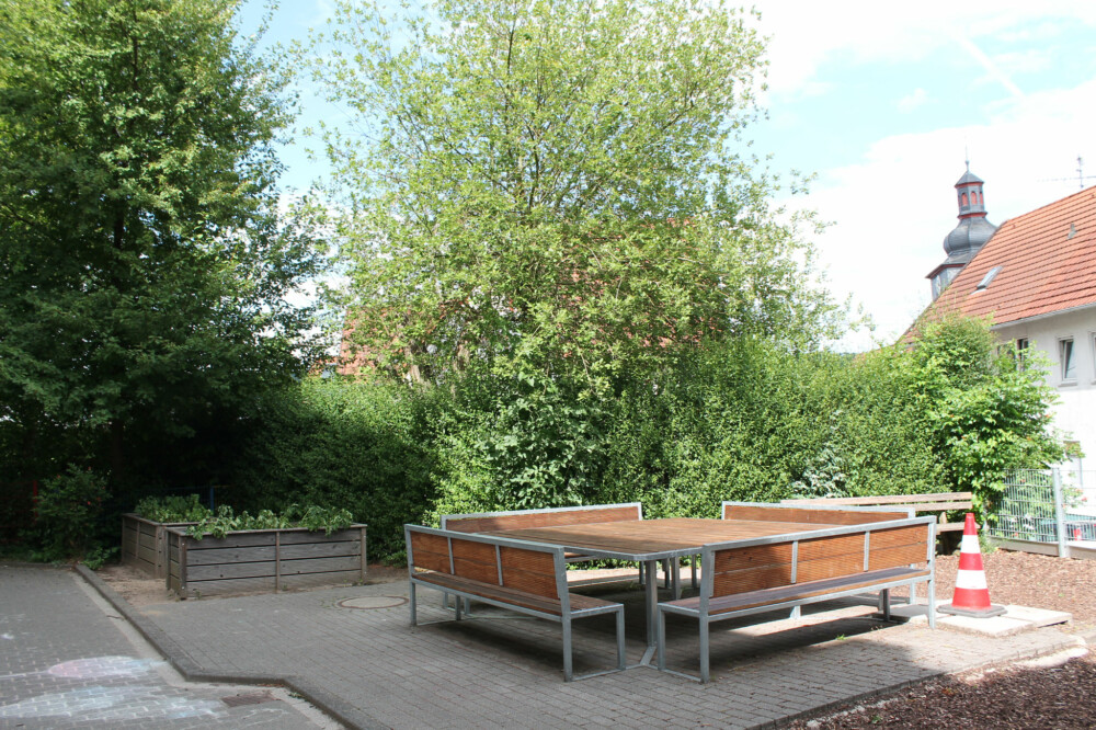 Bereich des Schulhofs mit Bäumen und Sitzbänken aus Holz und Metall.