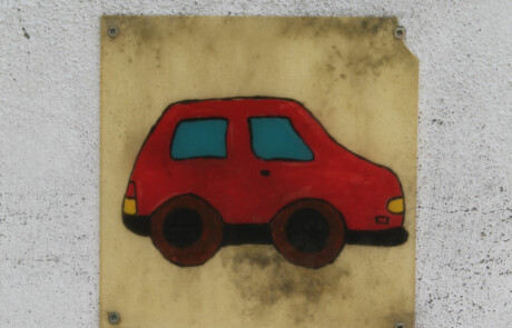Pausenhof Wandbild mit einem roten Auto aus Holz an einer hellen Mauer.