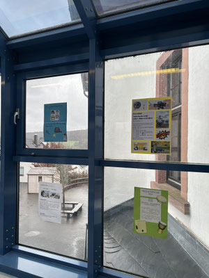 Projektwoche und Schnuppertag_2 Mehrere Informations- und Motivplakate hängen innen an einer verglasten Verbindungsgangwand über dem Schulhof.