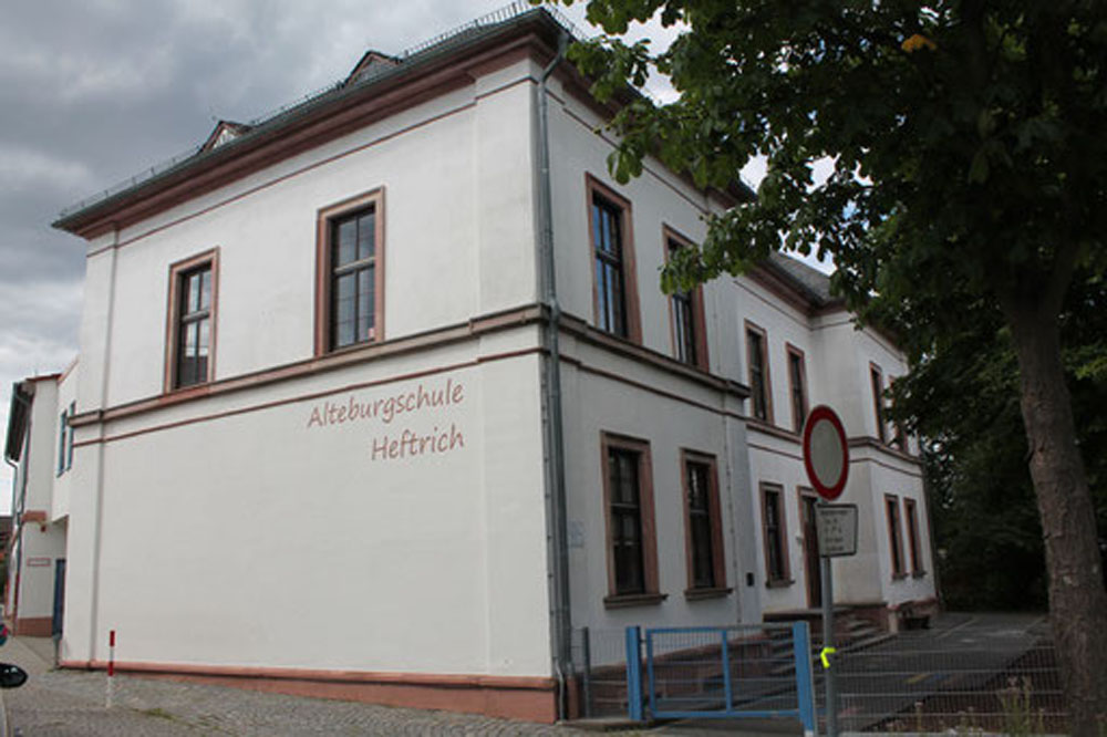 Seitliche Außenansicht der Alteburgschule Heftrich mit Bäumen und Schulhof.