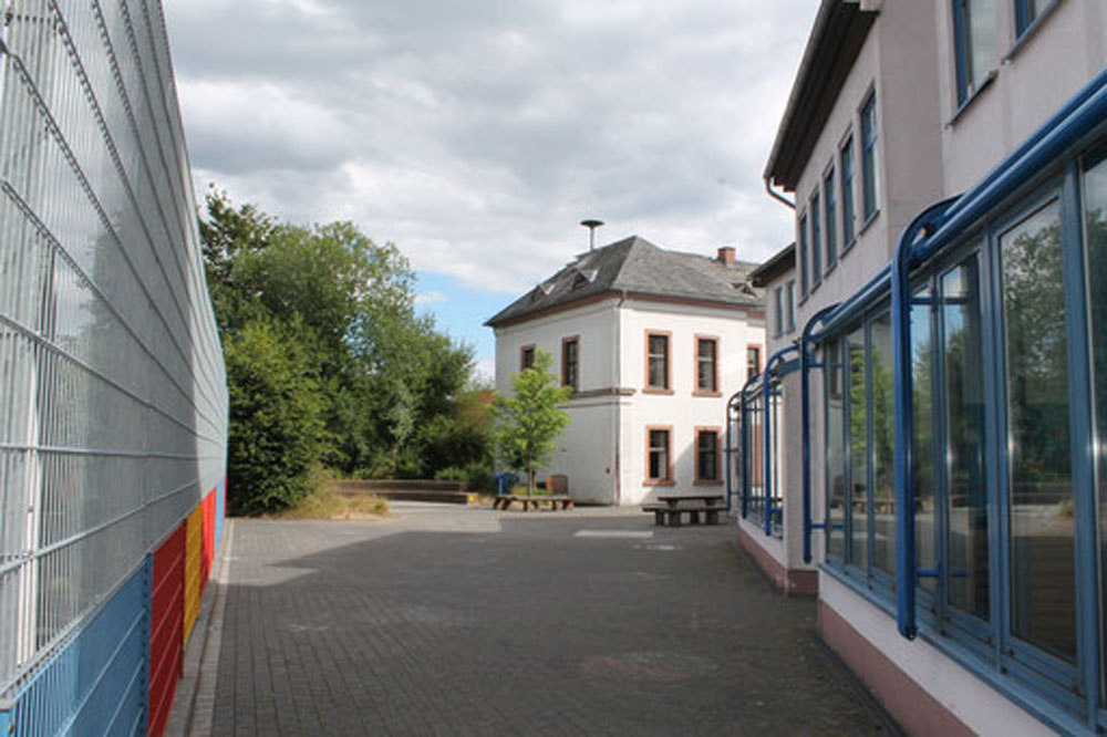 Außenansicht eines Schulgebäudes mit Bäumen und Metallzaun.