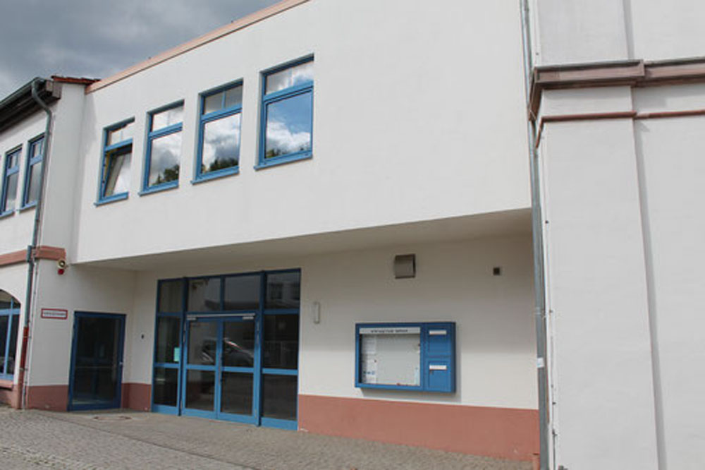 Schuleingang mit blauem Türbereich und überdachter Eingangszone.