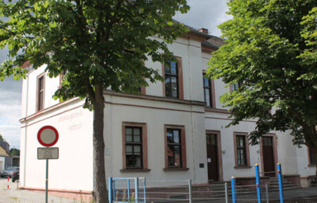 Schulgebäude_07 Außenaufnahme der Alteburgschule Heftrich mit Zaun und Bäumen.