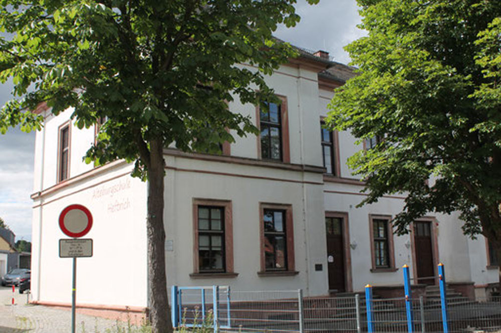 Außenaufnahme der Alteburgschule Heftrich mit Zaun und Bäumen.