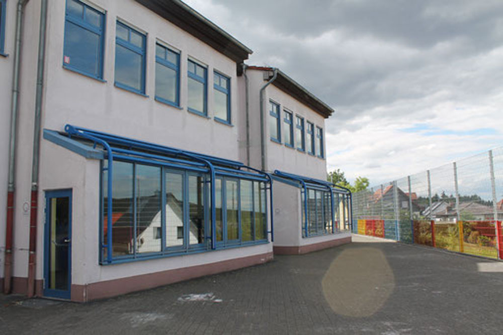 Außenansicht eines Schulgebäudes mit Bäumen und Metallzaun.