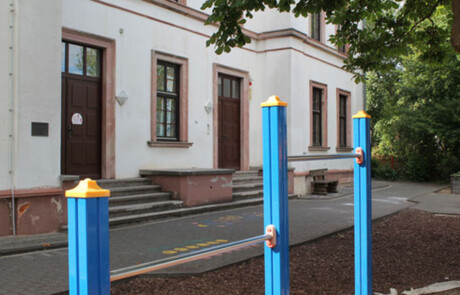 Schulgebäude_10 Schulhof mit blau-gelben Spielfigurenpollern vor der Alteburgschule Heftrich.