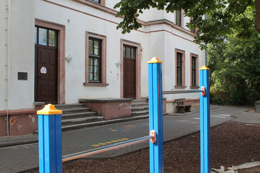 Schulhof mit blau-gelben Spielfigurenpollern vor der Alteburgschule Heftrich.
