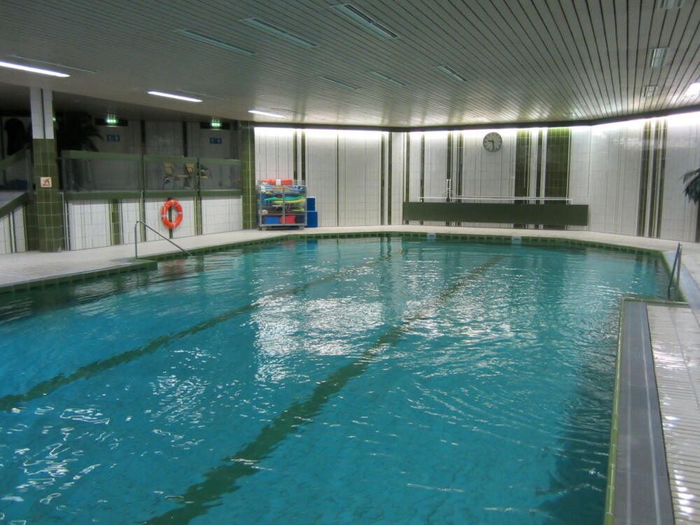 Innenaufnahme eines Hallenbads mit großem Schwimmbecken und umlaufenden Fenstern