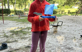 Kind hält ein selbstgebasteltes Boot auf einer Wiese.