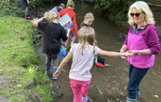 Kinder stehen mit Begleitpersonen im Bach und beobachten den Wasserlauf.