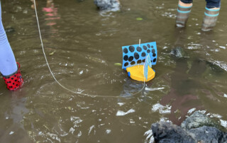 Gegenstände schwimmen an einer Schnur im flachen Bachwasser.