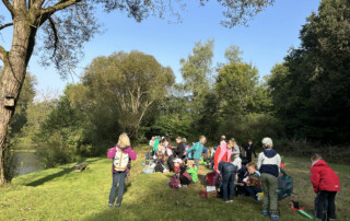 Kind hält ein gebasteltes Boot in den Händen und steht auf einer Wiese.