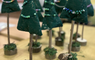Kleine Filz-Weihnachtsbäumchen mit Perlenketten stehen eng beieinander auf Holzfüßen.