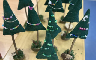 Mehrere gebastelte Filz-Tannenbäume mit bunter Perlendekoration auf einem Tisch angeordnet.