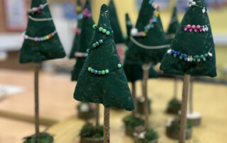 Gruppe von Filz-Tannenbäumchen auf Holzsockeln, verziert mit Perlen in verschiedenen Farben.