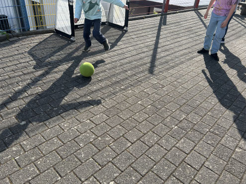 Kinder spielen mit einem Ball auf einem gepflasterten Schulhof.