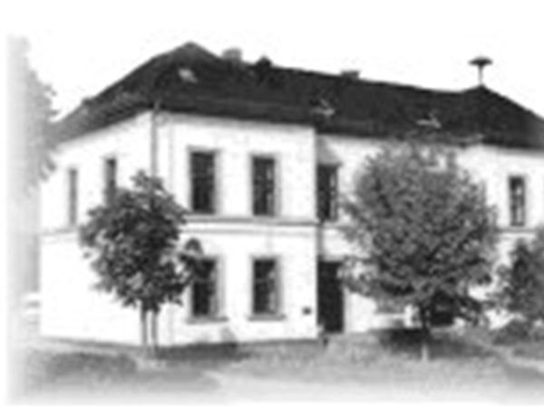 Altes Schwarz-Weiß-Foto des Schulgebäudes der Alteburgschule Heftrich, umgeben von mehreren Bäumen.